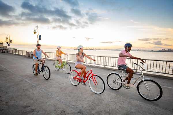 A group of bike riders pedaling down a boardwalk on their Schwinn cruiser bicycles while the sun sets.
