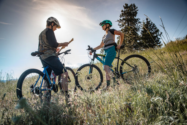 Two mountain bikers taking a break in the hot sun on a mountain bike trail.