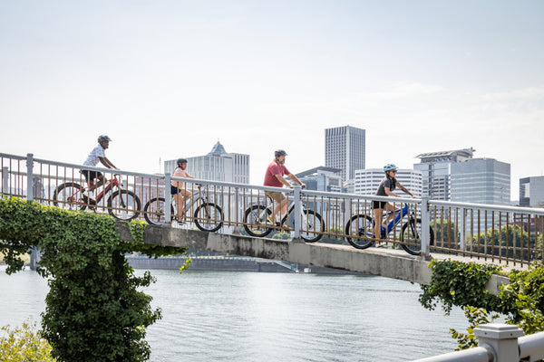 A group of bike riders pedaling down a ramp in a city while they all ride Schwinn e-bikes.