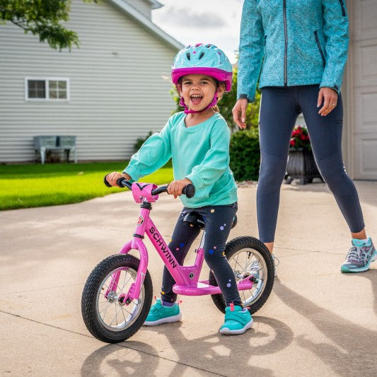 A young girl looking excited as she learns to ride her kids balance bike with her parents help.