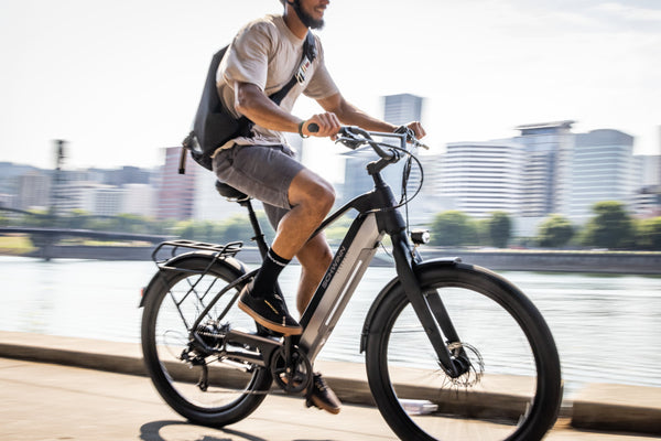 A man riding an e-bike on the sidewalk in the city.