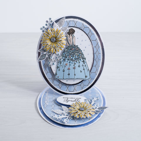 A beautiful layered oval card with blue and white card and a sparking geometric glitter background. The card features a sparkling yellow 3D flower with glitter foliage and a lady wearing a blue dress adorned with crystals.