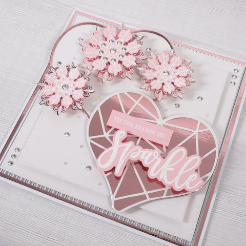 Learn how to create this pretty pink and rose gold heart Christmas Card featuring heart shaped layers and 3D paper snowflakes from Chloes Creative Cards.