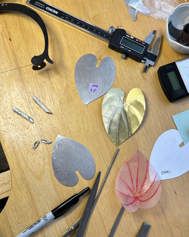 Photo of author's jewelry bench with the anthurium flowers in progress, and covered shapes in both metal and wax, and tools strewn about
