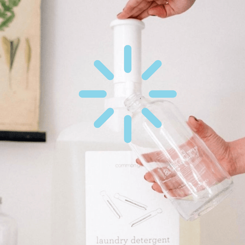 Person refilling a glass bottle of laundry detergent from a big container