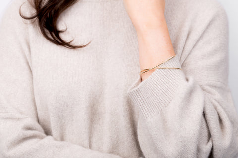 Model wearing a beige cashmere sweater with two delicate rose gold bangles by Natasha Sherling
