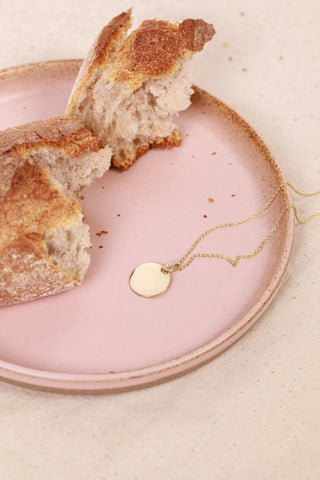 Pale pink plate with a torn baguette and gold necklace by Natasha Sherling