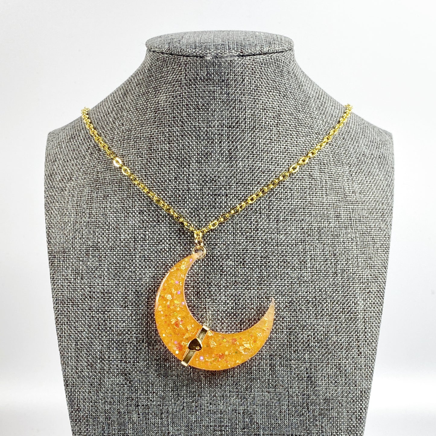 Golden Crescent Moon with Heart Resin Necklace on grey fabric display stand