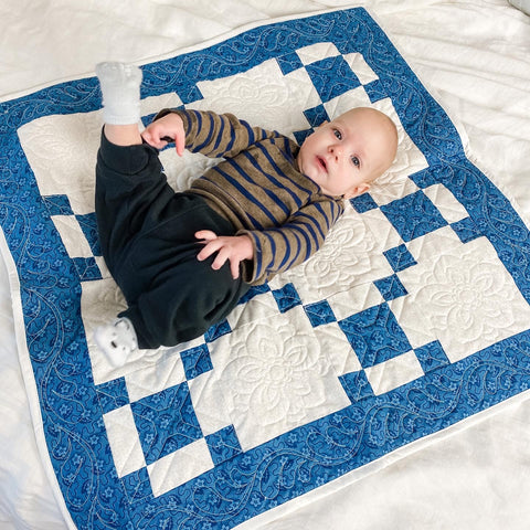 Baby laying on a small blue and white quilt