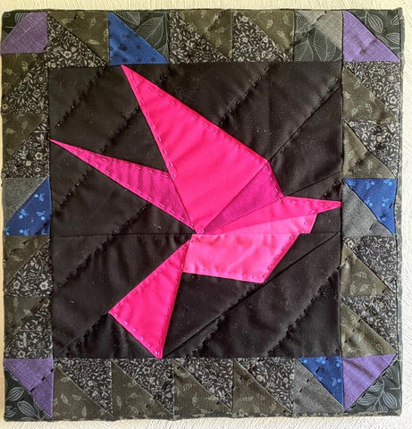 A pink quilted bird on a black background fabric attached with a wooden framed