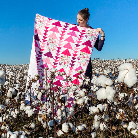 A quilt of pink triangles on a white background with a girl holding it in a field of cotton