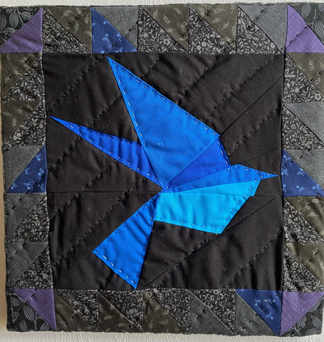 a blue bird, hand quilted with a black background on a wooden frame