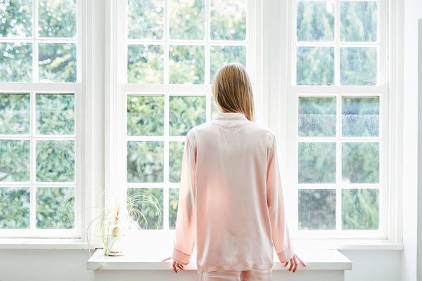 窓の外を眺めるパジャマ姿の女性