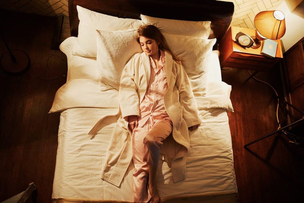 Foo Tokyoのシルクパジャマを着た女性がベッドに寝転がっている