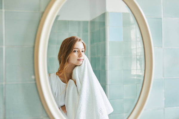 鏡の中の女性がタオルで顔をふく