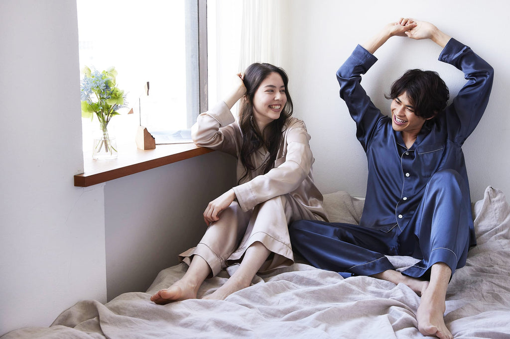 Foo Tokyoのシルクパジャマを着た男女がベッドで談笑している姿