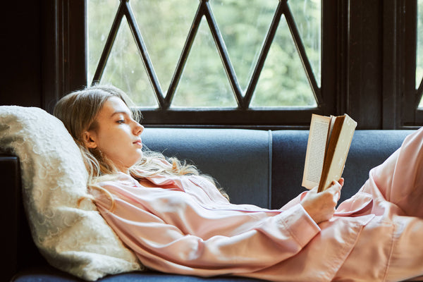 ソファで本を読むパジャマ姿の女性