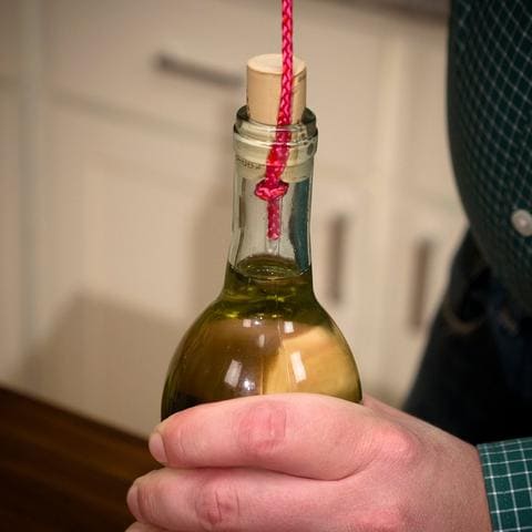 Elle enroule de la corde sur une bouteille de vin pour faire une
