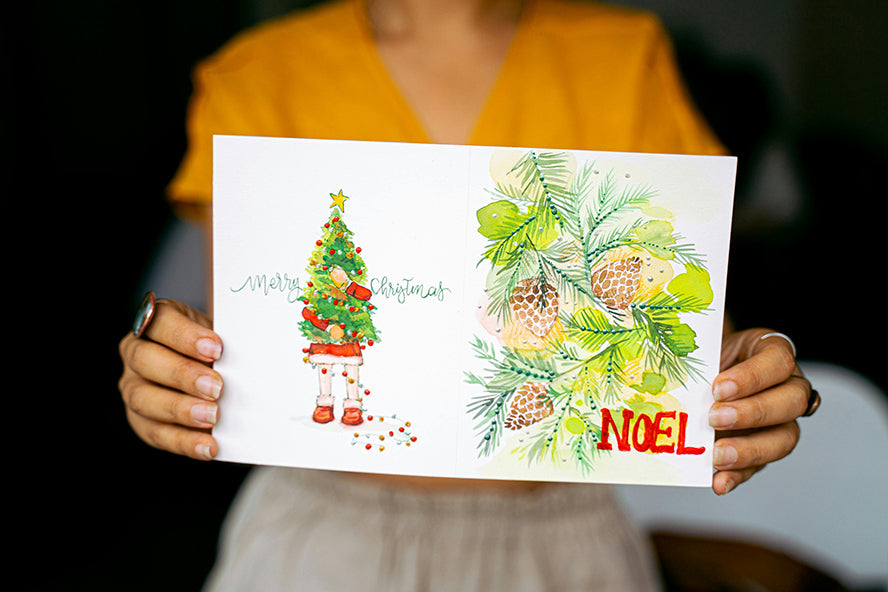 A person holding out a card that reads "Noel".