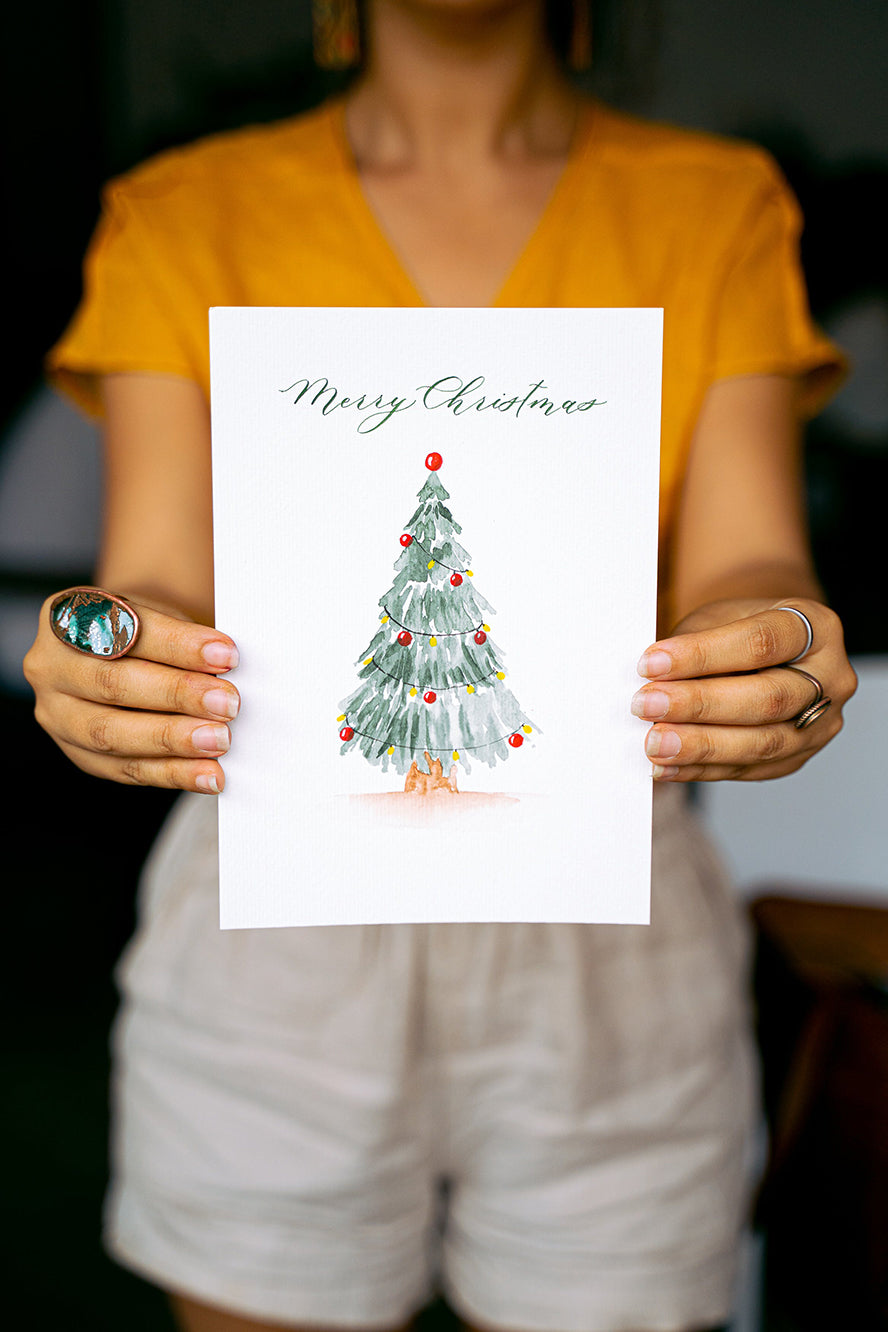 Person holding up a Christmas card with an illustrated Christmas tree on the cover.