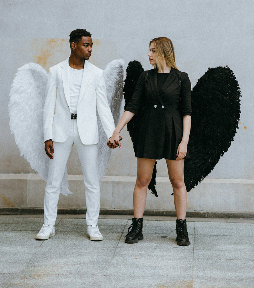 A man and woman holding hands each wearing angel wings.