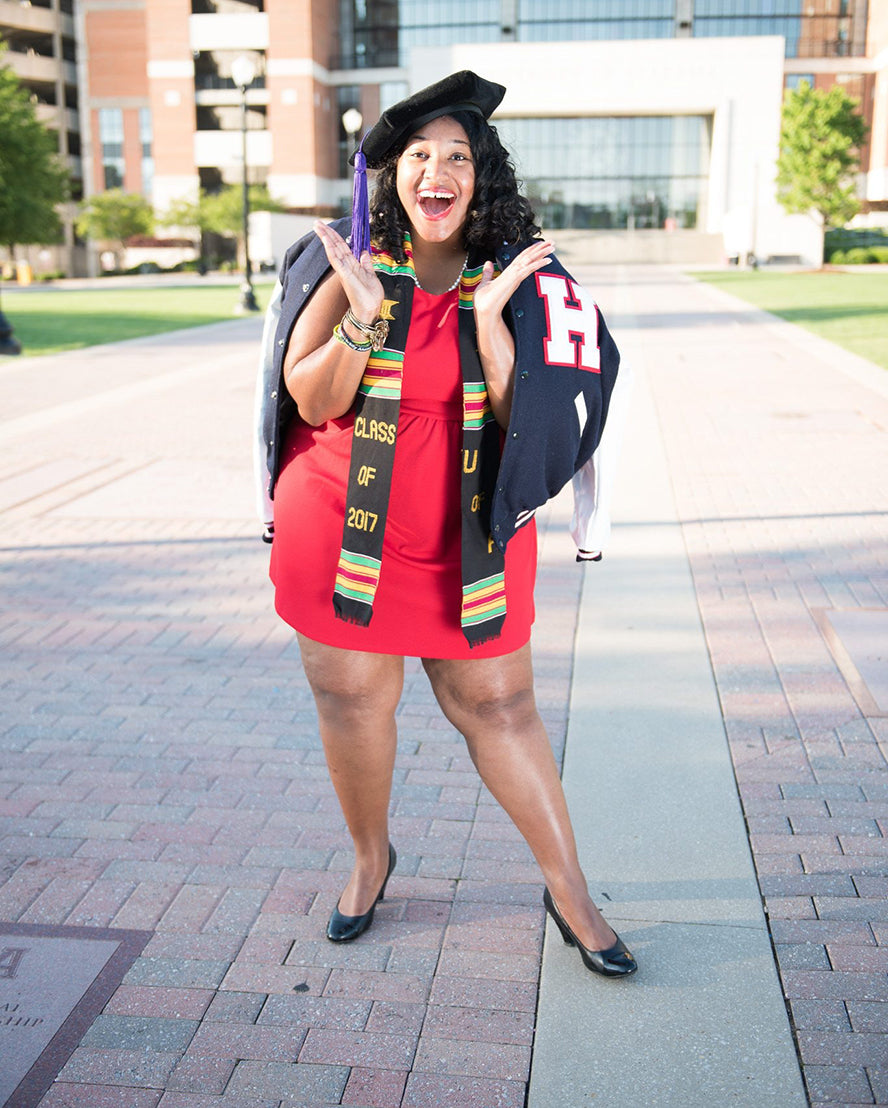 Woman with her hands thrown up posing for a fun solo graduation photo.