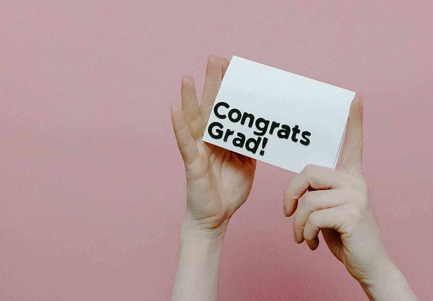 Hands reaching up holding a card that reads "Congrats Grad!"