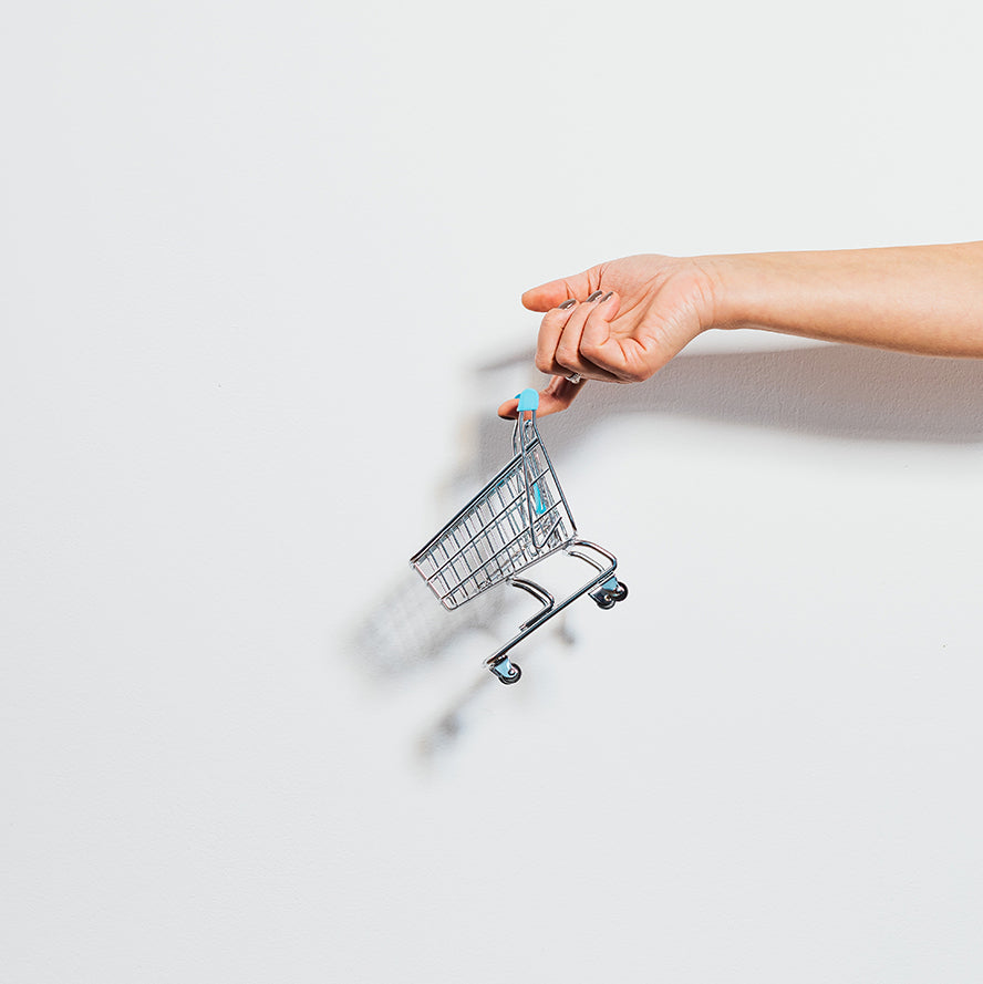 Shot of a hand over white, a tiny shopping cart hanging of the finger.