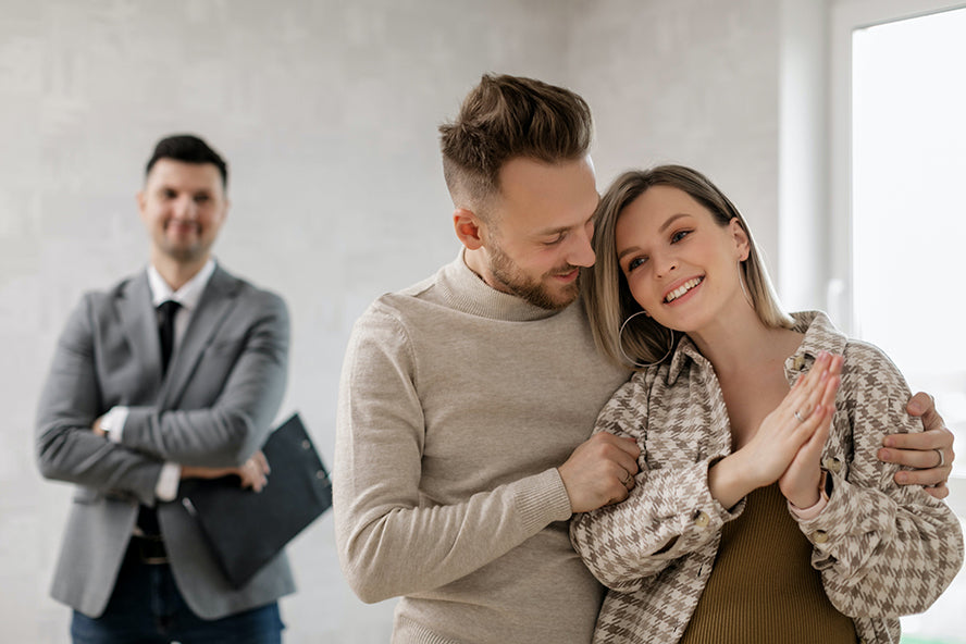 A happy couple embracing in their new home as their real estate smiles in the background.