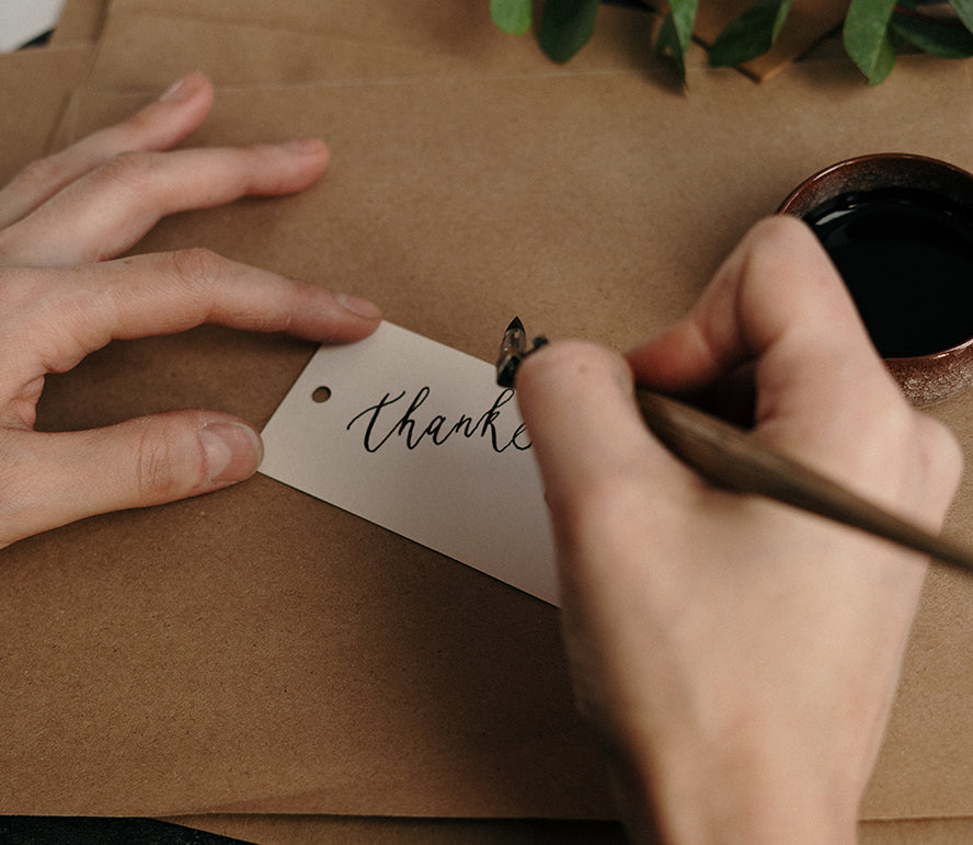 A person writing thank you in calligraphy.