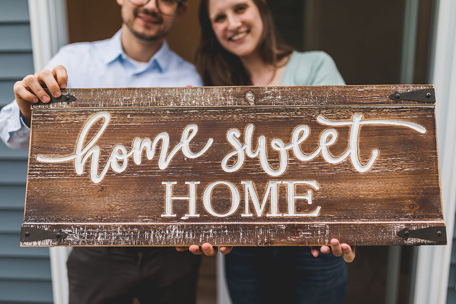 A couple holding up a wooden "Home Sweet Home" sign.