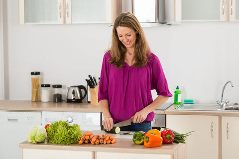 Smiling Woman Cutting Vegetable On Chopping Board In Kitchen