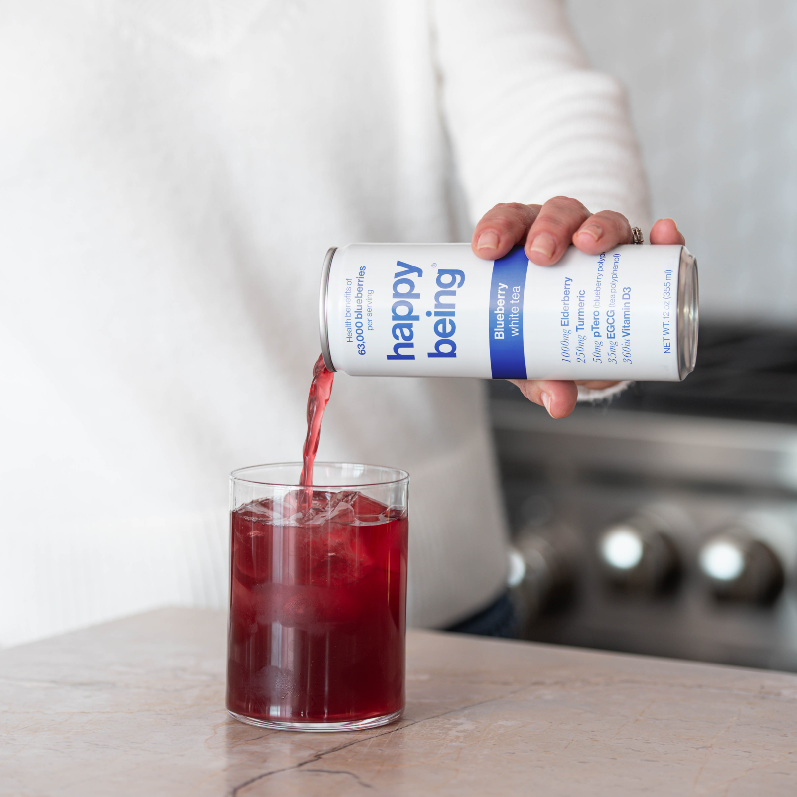 A person pours blueberry white tea from a 'happy being' can into a glass with ice.