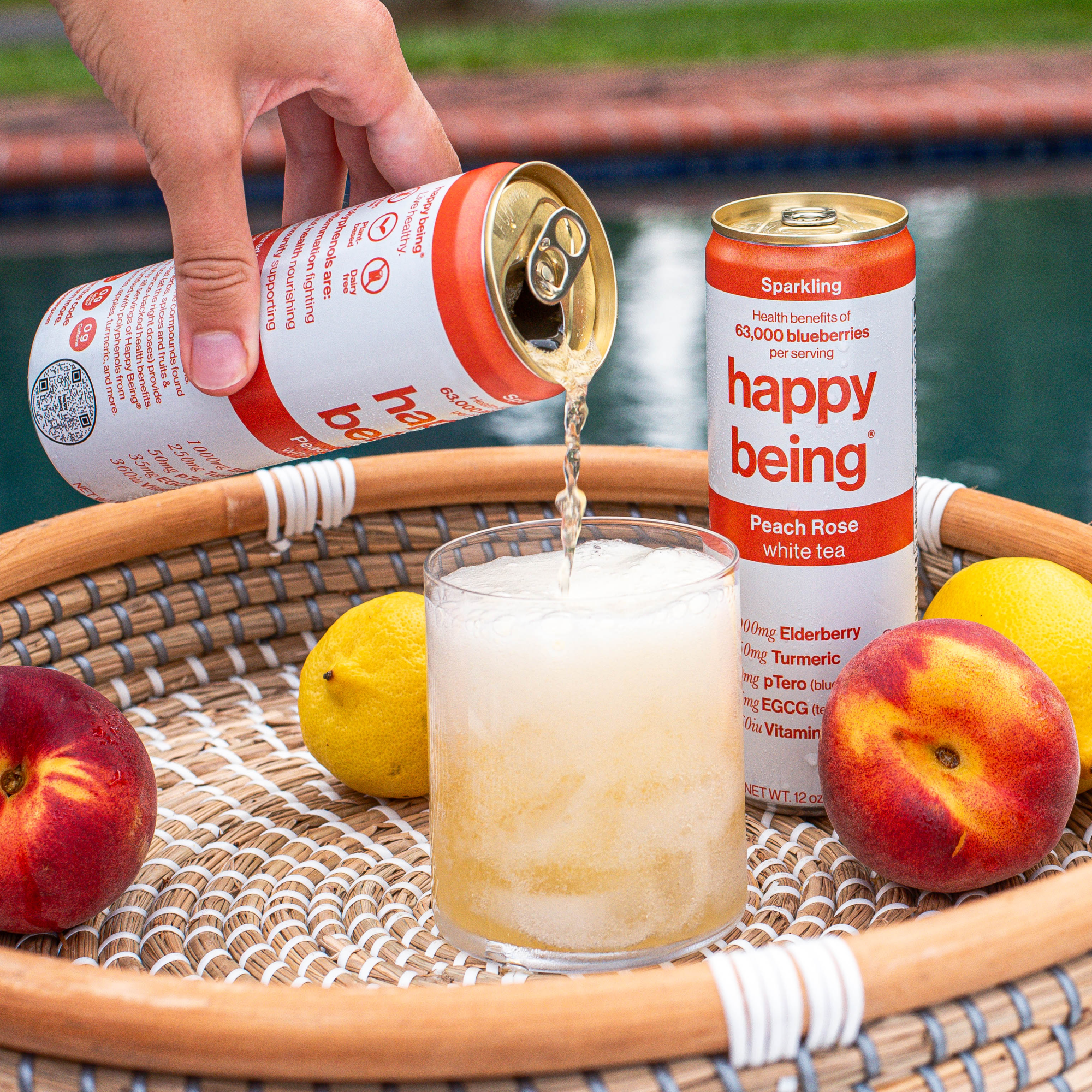 Pouring Happy Being Peach Rose tea into a glass on a wicker tray with fruits.