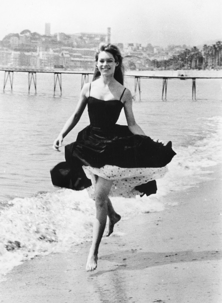 Brigitte Bardot, the iconic French actress, runs barefoot on the sandy beach in Cannes, gracefully swaying in a chic black dress with a petticoat underneath