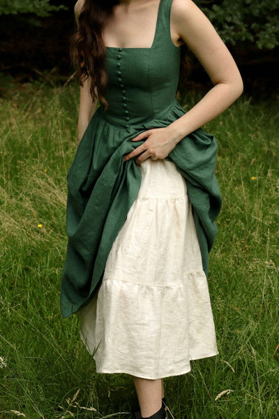 A girl in a field of grass in Germandy, lifting up her linen Gaâla dress to reveal a voluminous petticoat underneath.