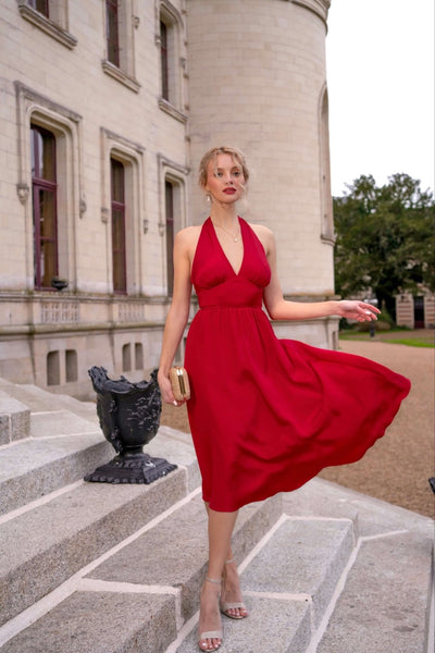 Blonde girl wearing a Marylin Monroe-inspired red halter dress, playfully swishing her skirt on the steps of an enchanting French castle.