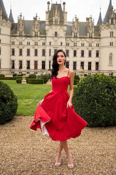 A brunette standing in front of a castle in France wearing a red Gaâla Brigitte Bardot inspired dress with petticoat.