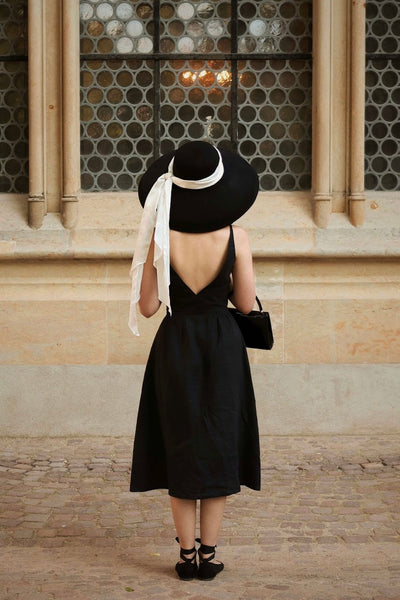Shirin Altsohn dressed up as Audrey Hepburn in Breakfast at Tiffany’s with her back to the camera wearing a large vintage hat and Gaâla black linen dress with V-neckline