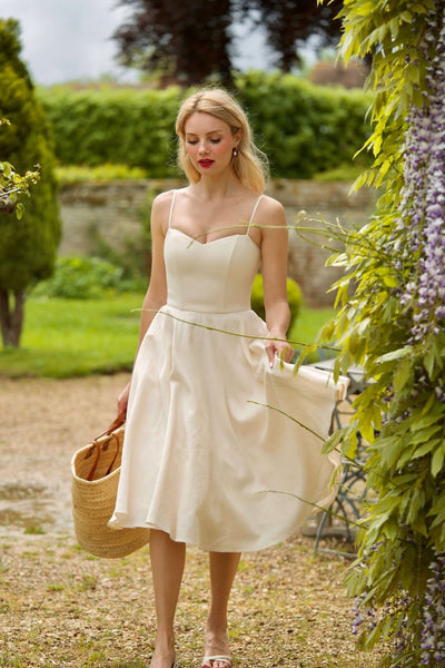 A beautiful blonde girl surrounded by enchanting flowers in scenic Normandy, wearing a cream colored corset dress with petticoat.