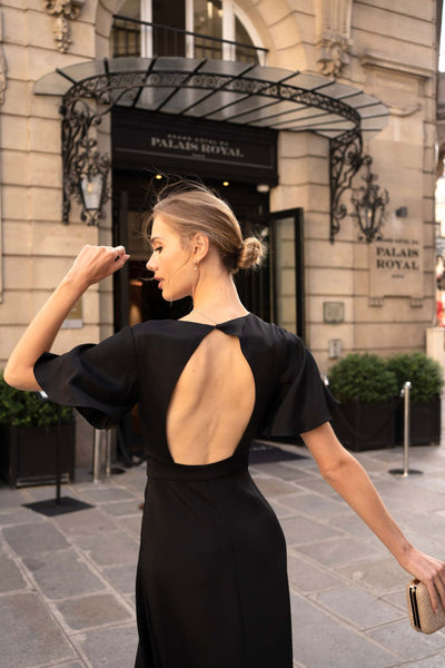 Blonde girl posting in Paris wearing a midi black backless silk Gaâla dress