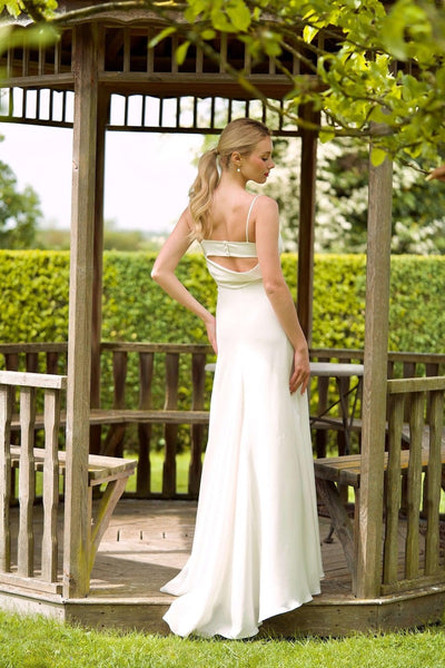 A blonde bride standing inside a gazebo in Normandy, France, wearing a maxi silk Gaâla wedding gown with a train.