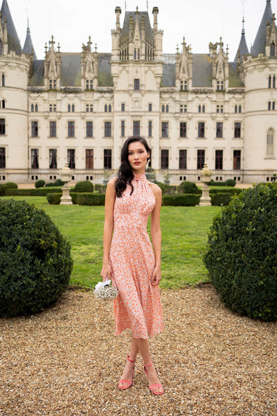 A graceful tall brunette girl, standing before a grand castle in France wearing a floral silk dress