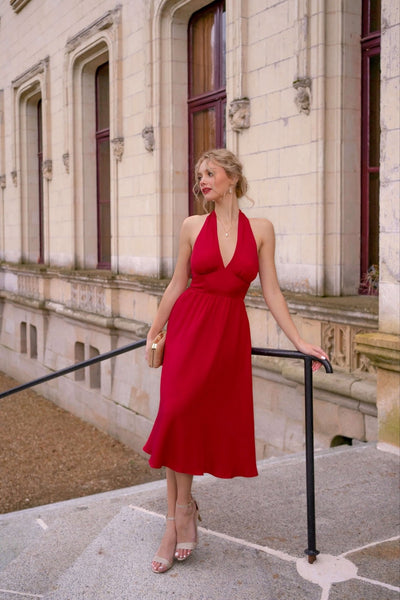 Blonde woman with elegant hair updo standing against a castle backdrop in France, wearing a vibrant red halter neck Marylin Monroe inspired Gaâla dress