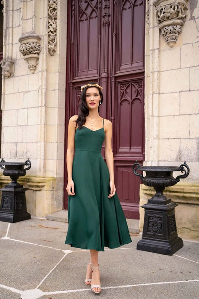 A graceful tall brunette girl, standing before a grand castle door in France wearing a long flowing green silk dress, wearing a crown of flowers in her hair