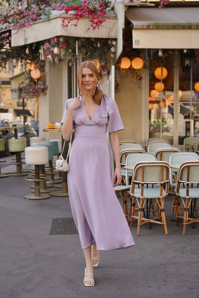 Smiling redhead woman wearing a lavender silk maxi dress with flutter sleeves, outside a charming Parisian café