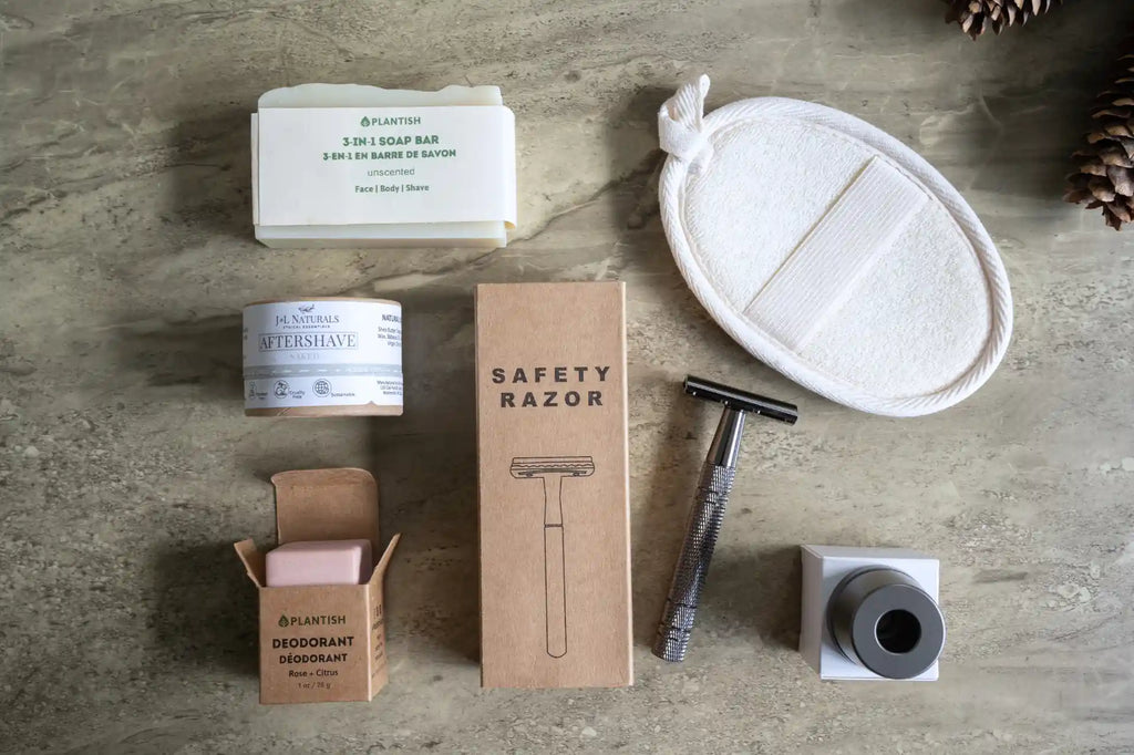 Metallic safety razor surrounded by aftershave rub, deodorant cube, loofah and soap bar on counter