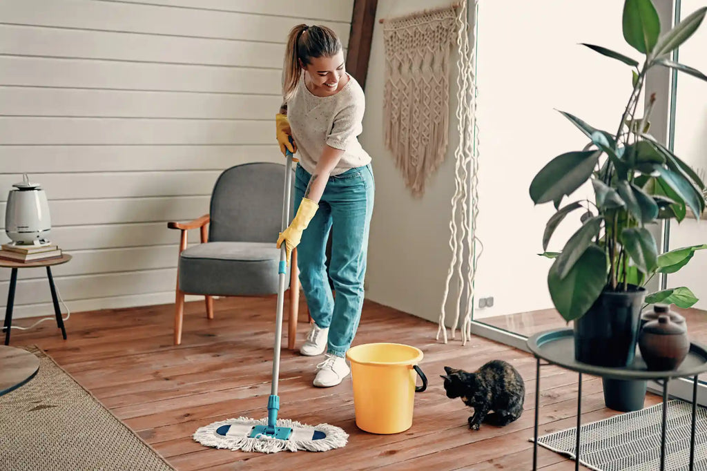 Woman in rubber gloves mopping wooden floor in living room