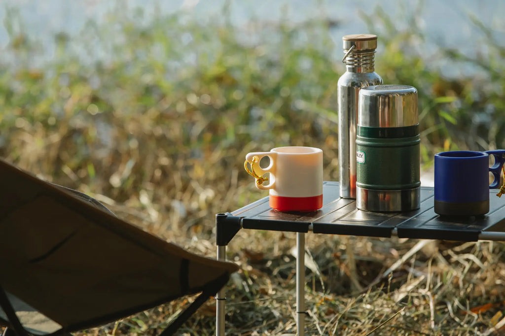 Close up of thermos and mugs on a small table next to a camping chair