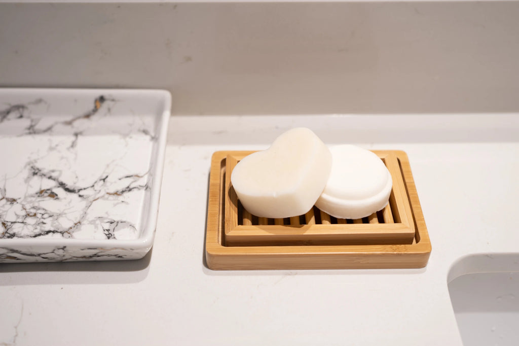 Shampoo and conditioner bars placed on a dual-layer bamboo soap dish, on a bathroom counter